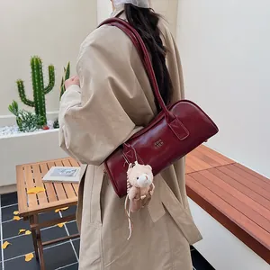 Detail der weinroten Boston Bag mit goldenem Logo und Bärenanhänger am Trenchcoat