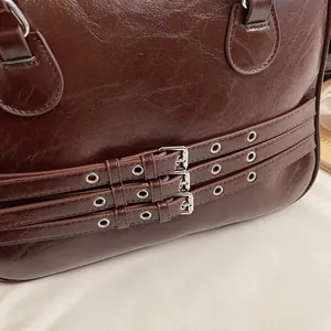 Dettaglio borsa in pelle cerata marrone scuro con tripla fibbia e finiture argento