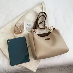 Detail of a beige tote bag featuring brown leather straps and elegant gold metal chain hardware
