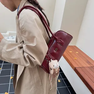 Detail einer dunkelroten Zylindertasche mit braunem Plüschbär-Anhänger am Trenchcoat