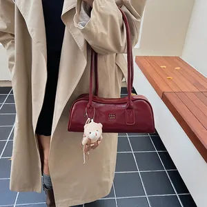 Detail der weinroten Boston-Tasche mit goldenem Logo und süßem Plüschbären am Riemen