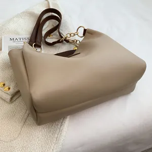Close-up of beige tote bag featuring brown leather straps and gold metal ring hardware