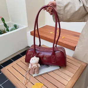 Dunkelrote Lackleder-Boston-Tasche mit süßem Plüschbären-Anhänger auf einem Holztisch