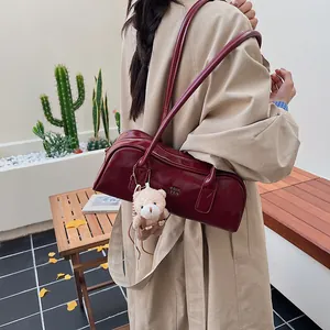 Detailansicht der weinroten Boston-Tasche mit Bärenanhänger und goldenem Logo-Akzent