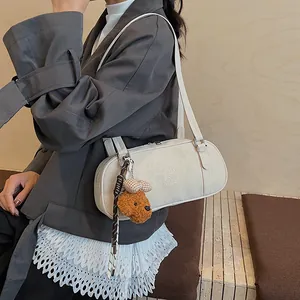 Nahaufnahme einer weißen Zylindertasche mit Logo-Prägung und Teddybär-Anhänger