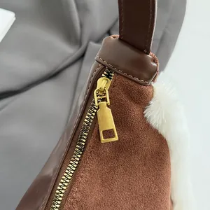 Detail of golden zipper and white faux fur trim on a brown suede shoulder bag