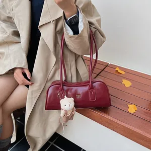 Detail der burgunderroten Boston-Tasche mit Goldlogo und niedlichem Bärenanhänger