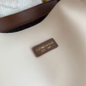 Detail of premium cream leather tote bag featuring a gold embossed dark brown brand logo plate