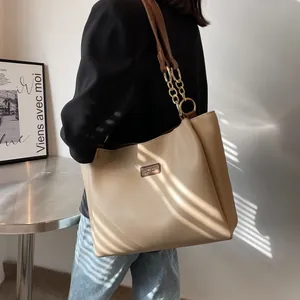 Detail of stylish beige tote bag with brown leather straps and gold chain accents