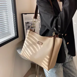 Chic cream tote bag with brown straps and gold chain detail on a model in soft light
