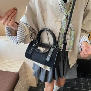 Close-up of black cylinder handbag with heart buckle and silver rivets shown on model