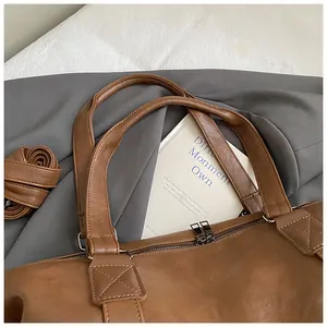 Detail of a brown leather travel tote with sturdy handles and adjustable shoulder strap