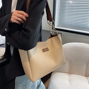 Detail view of large beige tote bag with brown straps and gold chain on model's shoulder