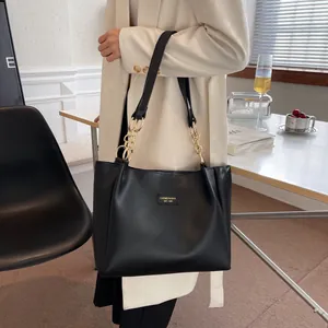 Close-up of a black matte leather tote bag featuring a gold brand plaque and chain strap