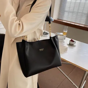Detail of black leather tote bag with gold chain strap shown in an office setting