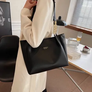 Detail of black leather tote bag with gold chain and logo patch on model in cafe setting