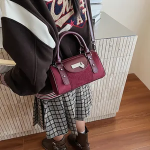 Detail of burgundy Boston bag with suede panels, silver metal bar and heart pendant
