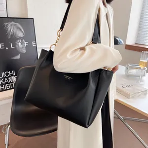 Close-up of a large black tote bag with gold chain strap detail on a white blazer