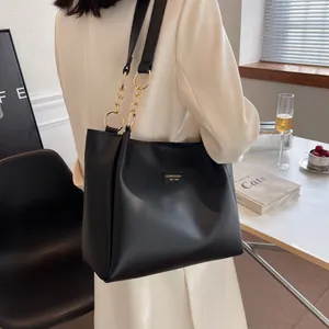 Detail of black tote bag with gold chain strap and brand plaque on beige blazer