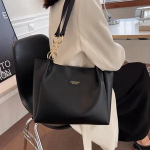 Detail of black tote bag with gold chain strap and logo on minimalist blazer outfit