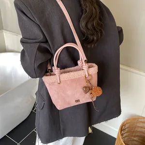 Detail der rosa Wildleder-Beuteltasche mit Lammfellbesatz und Metall-Logo am grauen Blazer