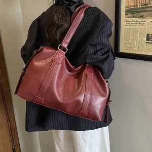 Close-up of wide reinforced straps and leather texture on a deep red travel tote bag