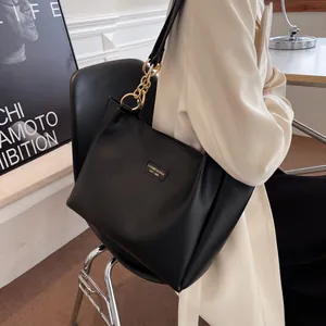 Detail of the black leather tote bag featuring a golden chain buckle and metal brand nameplate