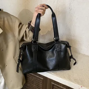 Detail of a black leather tote bag with long handles and decorative side straps