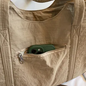 Detail of khaki nylon tote showing a front zipper pocket with a phone for storage capacity