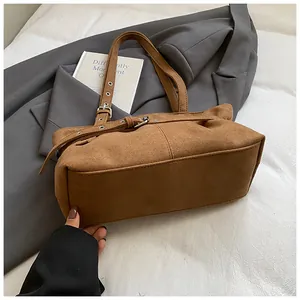 Detail of brown suede tote bag with decorative belt buckle and silver metal eyelets