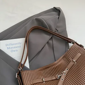 Detail of brown pleated PU leather shoulder bag with silver rings and straps on grey suit