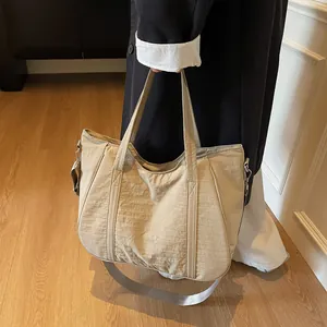 Detail shot of a large beige tote bag featuring a removable wide strap and nylon texture