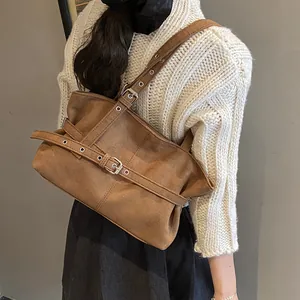 Close-up of vintage brown suede tote bag with belt buckle details worn over a beige sweater