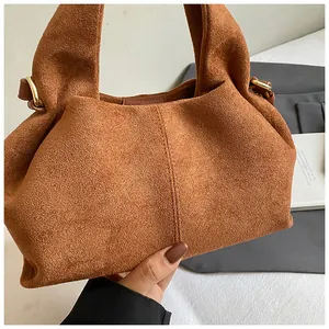 Detailed close-up of brown suede handbag with minimalist stitching and gold metal hardware