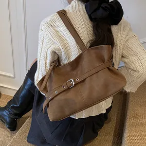Close-up of brown suede tote bag with decorative silver buckle belt on a white sweater