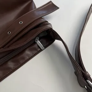 Detail of dark brown leather tote bag showing silver zipper and metallic eyelet decor