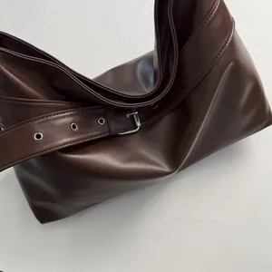 Detail of dark brown leather tote bag showing wide strap with silver buckle and eyelets