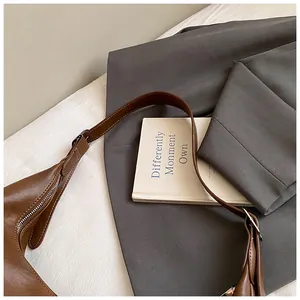Détail du sac hobo en cuir marron avec fermeture éclair argentée sur fond de costume gris