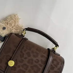 Détail du sac à main léopard marron foncé avec boucles dorées et charmant petit chien peluche