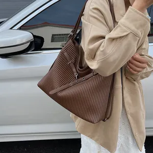 Detail of dark brown pleated hobo bag with silver eyelets on a beige trench coat