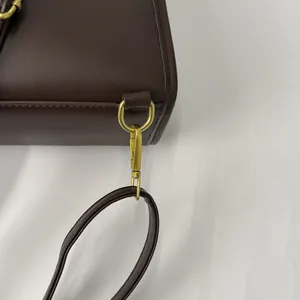 Détail de sac en cuir marron foncé avec anneau en D et fermoir mousqueton en métal doré vieilli