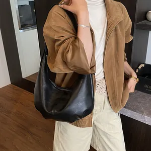 Détail d'un grand sac hobo en cuir noir porté avec une veste en daim marron