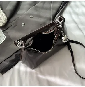 Detail of glossy brown underarm bag with silver zipper and metallic ball pendant