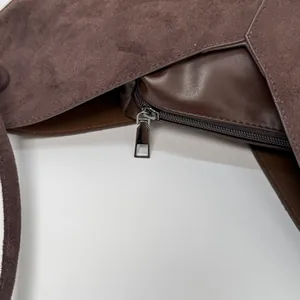 Détails de couture sur daim marron foncé et fermeture éclair métallique d'un sac cabas