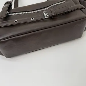 Detail view of deep brown PU leather shoulder bag featuring silver metal zippers and buckles
