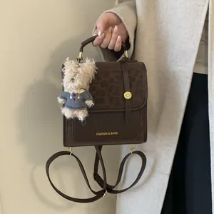 Détail du sac à dos en cuir marron avec rabat léopard et breloque ours en peluche