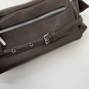 Detailed close-up of dark brown leather texture with silver zipper and buckle accents