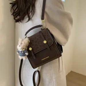 Sac bandoulière marron avec rabat léopard et pendentif ours sur un manteau beige