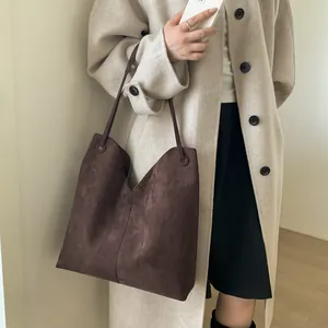Gros plan d'un grand sac cabas marron en daim mat porté à l'épaule par un mannequin élégant