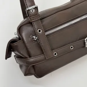 Detail of dark brown leather handbag featuring silver zippers and metallic grommets